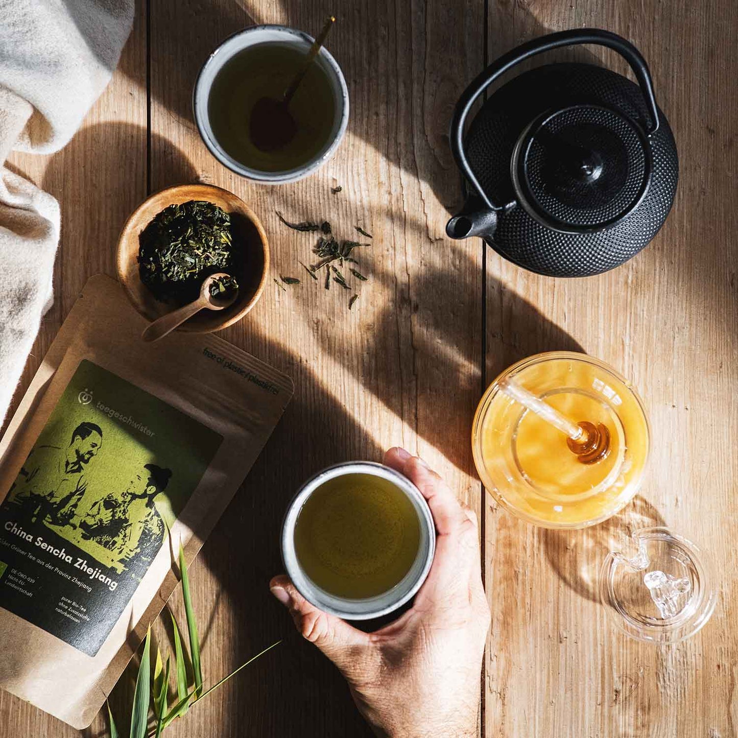 Auf diesem Bild sieht man die Verpackung des China Sencha mit losem Tee und einen Aufguss in einer Teekanne.