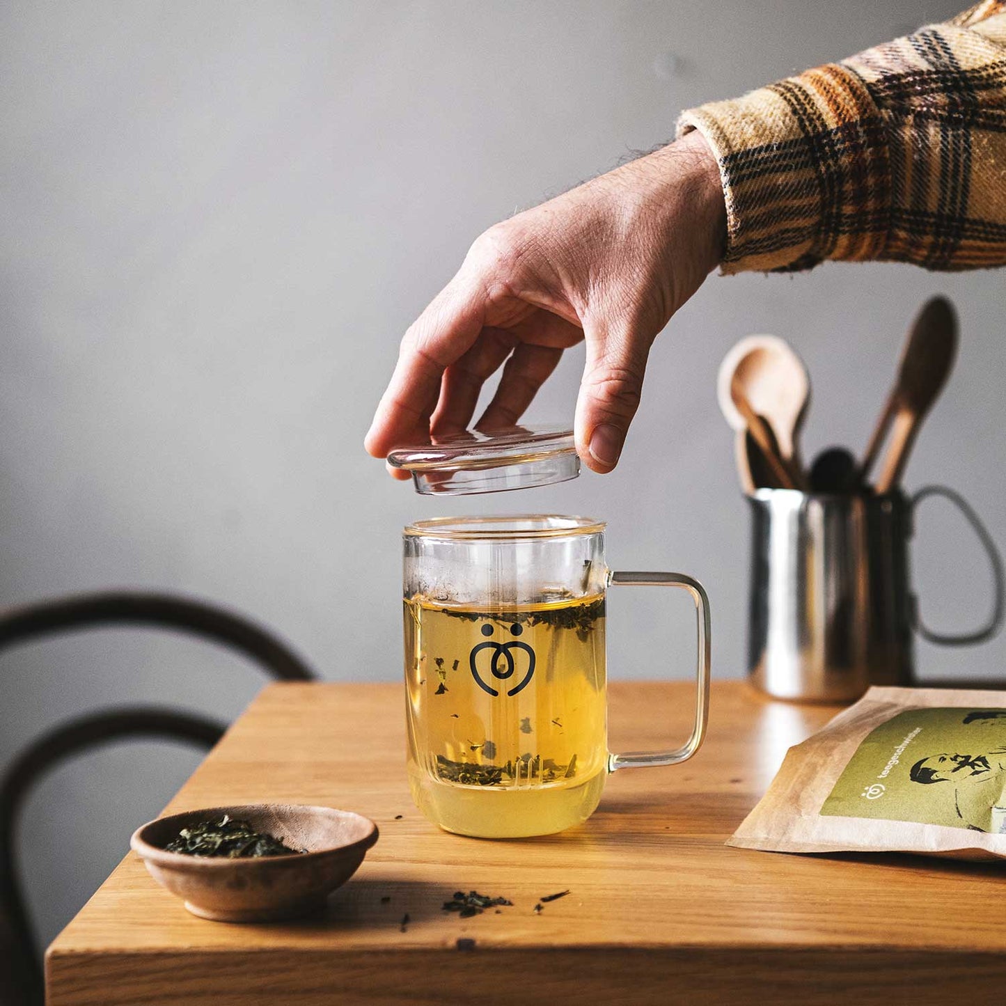 Hand hebt den Deckel des Teeglas mit Sieb an. Im Glas befindet sich Tee.