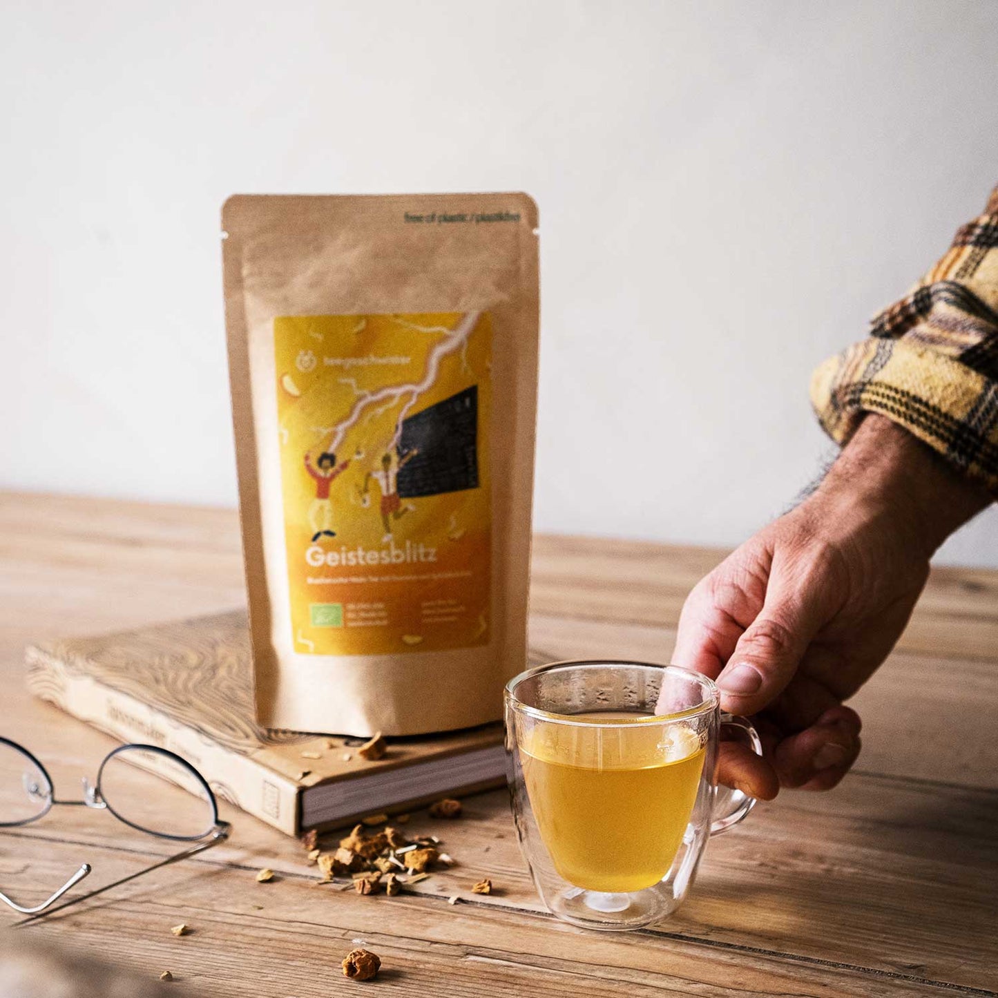 Dieses Bild zeigt die Teeverpackung und eine Hand die den aufgegossenen Guarana Tee hält.