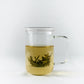 Teeglas auf weißem Hintergrund mit aufgegossenem Tee mit geschlossenem Deckel und Sieb im Glas.