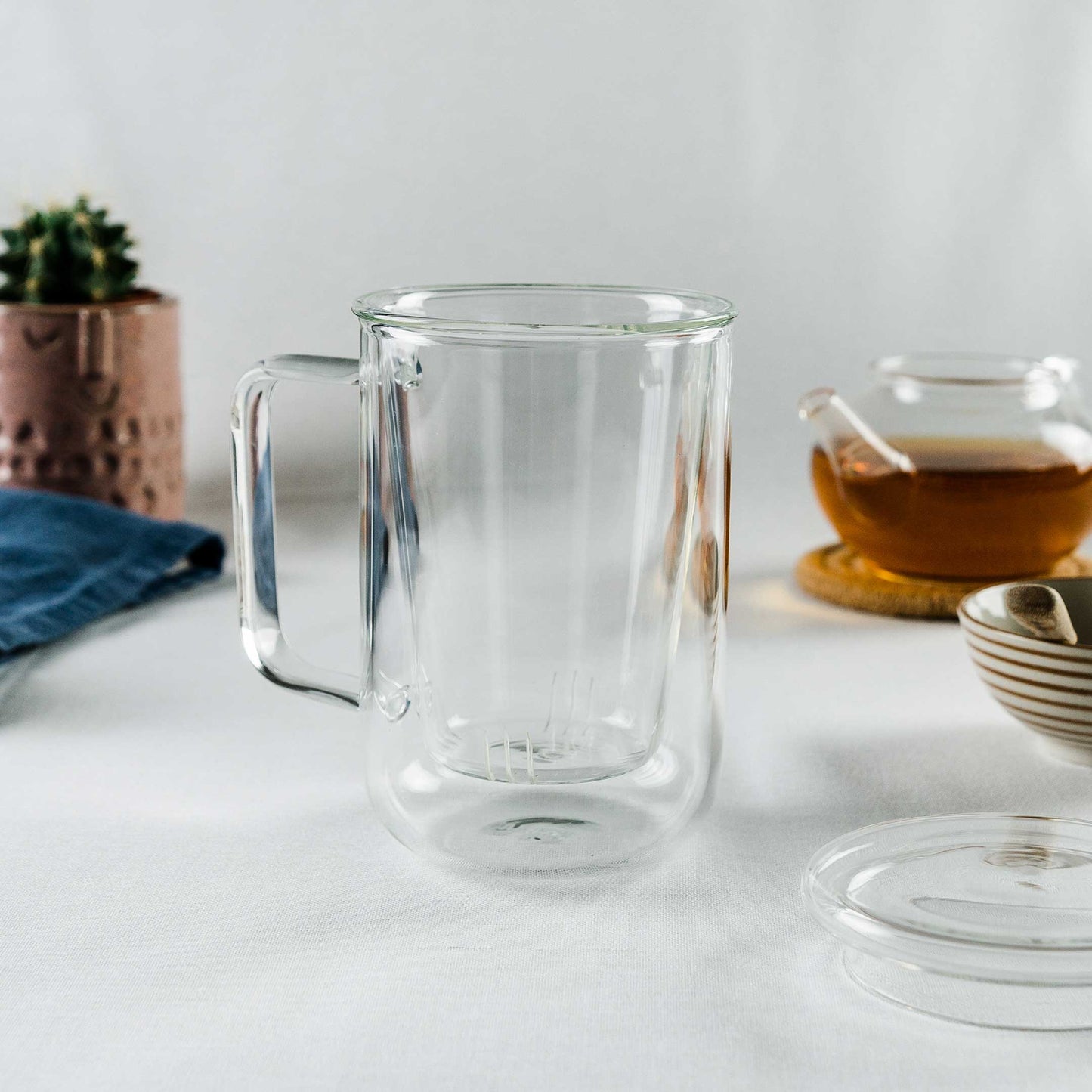 Leeres Teeglas mit Sieb im Glas mit Teekanne und Tee im Hintergrund.