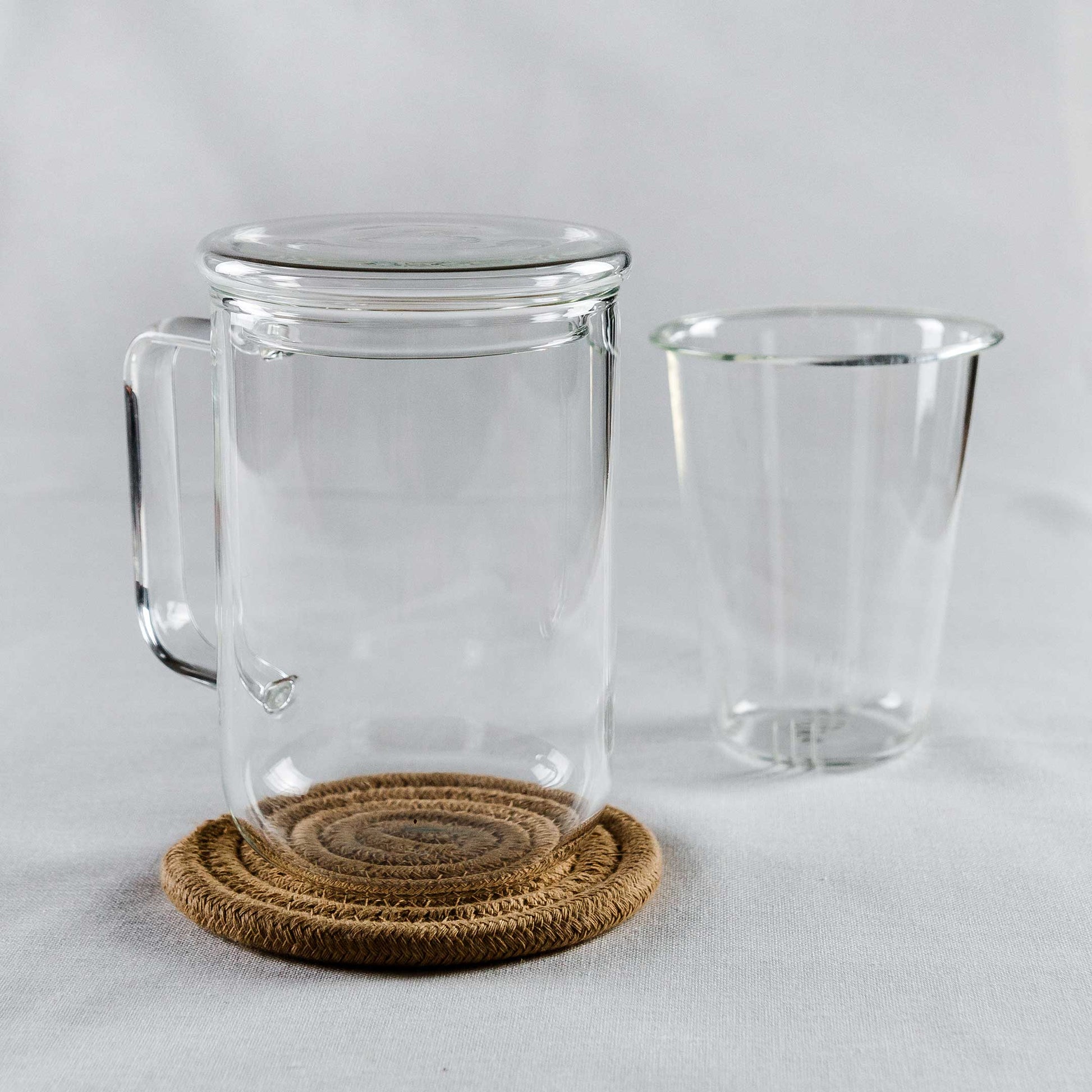 Teeglas mit Deckel auf einem Untersetzer mit Sieb neben dem Glas.